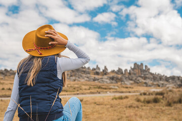 A woman wearing a yellow hat is sitting in a field. Huayllay Stone Forest, Peru.