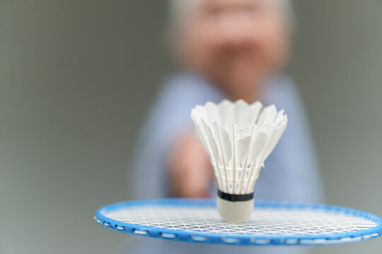 Selective focus of shuttlecock and badminton racket with blurred Asian senior sportswoman in background