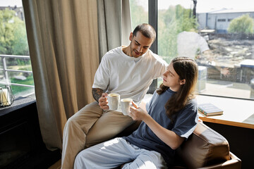 A young gay couple enjoys a morning coffee together in their modern home, filled with natural light.