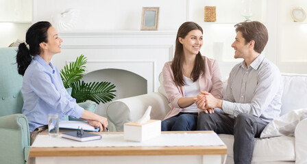 A young couple sits closely, hand in hand, sharing their journey with a woman psychologist in a session filled with empathy and constructive dialogue.