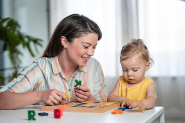 A young mother is playing with her young toddler daughter at home