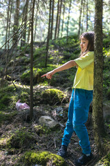 A girl points her finger at a plastic bag in the forest.