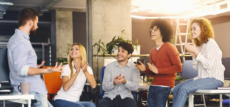 A casually dressed diverse group of colleagues is gathered in a brightly lit modern office, clapping and smiling, showing support and appreciation during an engaging team meeting