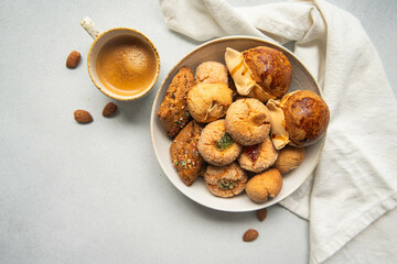 Variety of homemade Italian sweets typical for Sardinia region. Pardulas, amaretti, papassine and pizzicchi in bowl and espresso on white table.