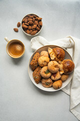 Variety of homemade Italian sweets typical for Sardinia region. Pardulas, amaretti, papassine and pizzicchi in bowl and espresso on white table.
