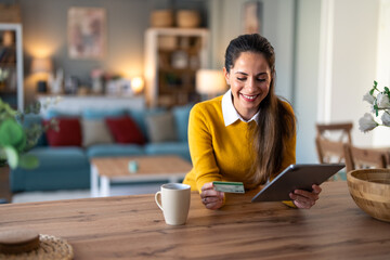 Happy young businesswoman holding credit card and looking at digital tablet pc while sitting at desk in a home office.