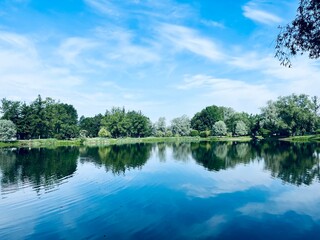 Beautiful tender blue sky reflection on the lake surface, trees silhouettes reflection on the lake surface, summer lake in the park