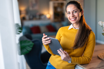 Smiling confident businesswoman looking at camera and holding digital tablet, posing for a business portrait photo.