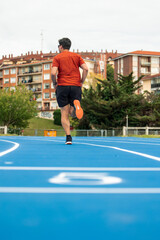 Fototapeta premium vertical Rear View of Male Runner Jogging on Blue Athletic Track