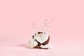 Coconut with splashes of water and white flowers on a pink background