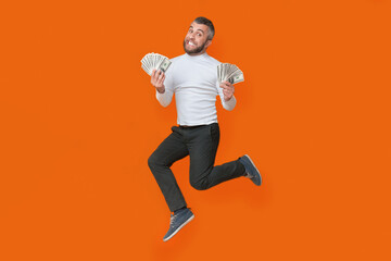 A man energetically jumps in the air, holding a bunch of money tightly in his hands. He appears to be celebrating or expressing joy over his financial success.