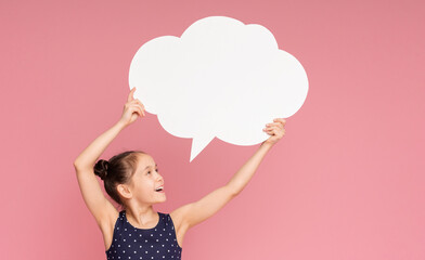 Happy little girl with raised hands holding blank speech bubble, pink studio background