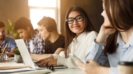 Students studying in library classroom, work on project on laptop and discuss