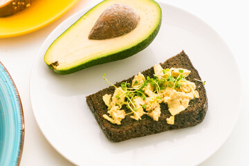 Avocado on toast or slice of rye bread with sliced avocado on a white plate on a light background. Close-up.