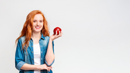 A woman is holding a vibrant red apple in her hand. She is looking at the apple with interest. The background is simple and unobtrusive, copy space