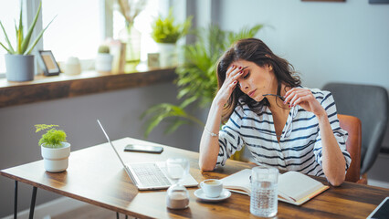 A thoughtful Caucasian businesswoman absently holds her glasses while reviewing documents beside...