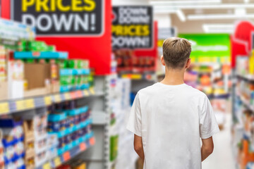 One young man walks along the shelves in a supermarket.
