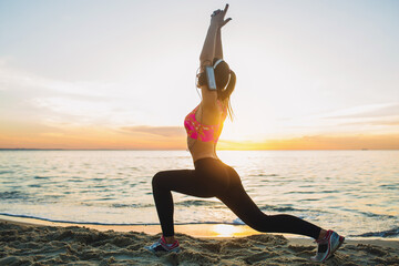 young woman doing sport exercises on sunrise beach in morning
