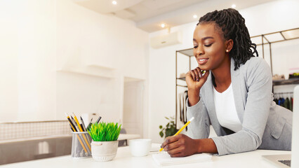 African American woman sits at a wooden desk, focusing intently as she writes on a piece of paper....