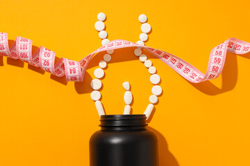 Black plastic jar, pills and measuring tape on yellow background, top view