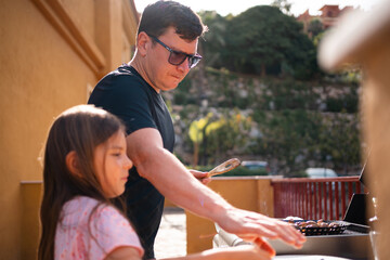 A father and daughter grilling vegetables together on a gas grill, focusing on the cooking process