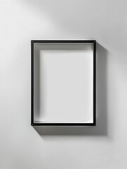Minimalist empty black picture frame on a gray wall casting a shadow, perfect for art or photo display in a modern setting.