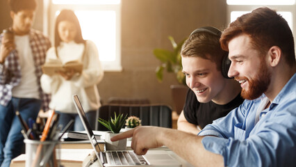 University students at library studying together, connecting online and pointing at laptop's screen, free space