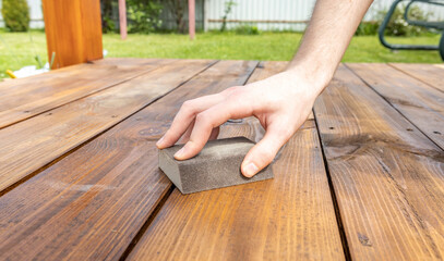A hand carefully sands a wooden deck with a sanding block, preparing it for a fresh coat of stain.