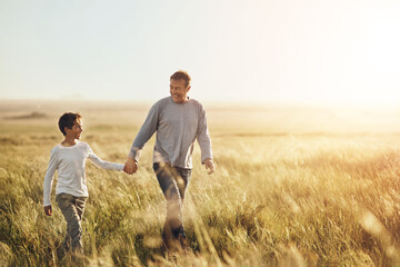 Holding hands, walking and father with child in nature at sunset for bonding together on vacation. Happy, farm and dad with boy kid on adventure, holiday or weekend trip in agriculture countryside.