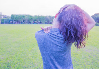 A woman shows signs of pain and stiffness in her body muscles, neck, and shoulders in an outdoor...