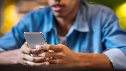 Cropped of black guy is seated at a table, engrossed in his cell phone. He is focused on the...