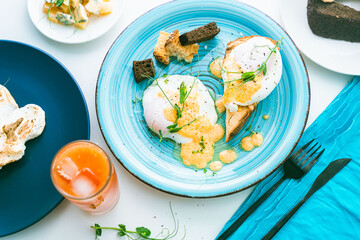 Poached egg toast with hollandaise sauce with peas and croutons on a turquoise plate and orange juice. View from above. Close-up.