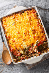 John Wayne Casserole is a taco beef casserole cooked in biscuit dough with sour cream, Cheddar, tomatoes and bell peppers closeup on the baking dish on the table. Vertical top view from above