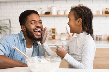 A fun moment captured as an african american father and his daughter have a playful flour fight in the kitchen, symbolizing joy and parenthood