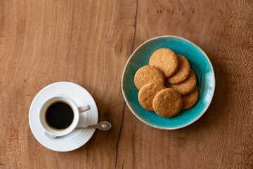 A cup of espresso next to a pate of biscuits on a wooden table