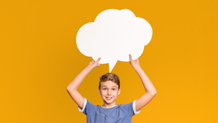 Inspired teenage boy having idea, holding blank speech bubble above his head, orange studio background