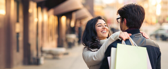 A man and woman are walking on a busy city street, both holding shopping bags in their hands.