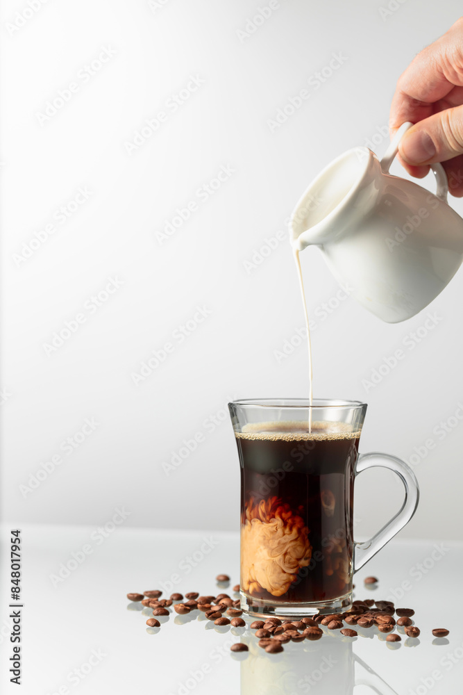 Wall mural a man's hand pours cream into a glass of coffee.