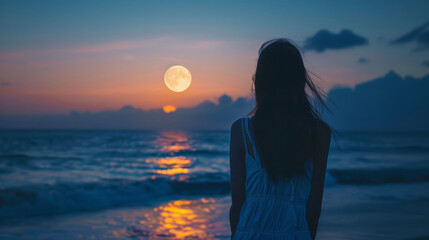 Woman standing on beach looking at full moon over ocean
