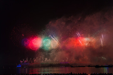  a vibrant fireworks display over water with multiple boats, showcasing a spectrum of colors and reflections creating a festive, celebratory atmosphere.