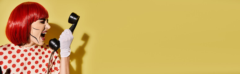 A creative redhead woman with pop art makeup holds phone in a playful manner on a bright yellow background.