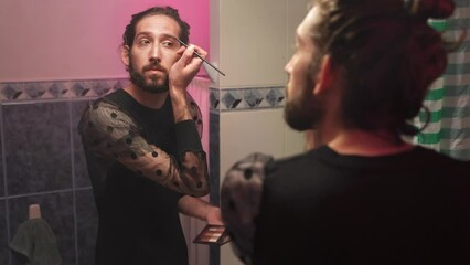 Gay queer man non-binary apply face skin makeup on eyelash at home. Real LGBT person - Powered by Adobe