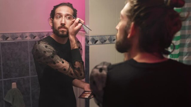Gay queer man non-binary apply face skin makeup on eyelash at home. Real LGBT person 