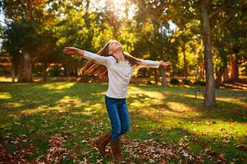 Girl, child or freedom in park with leaves for adventure, fun activity or spinning with enjoyment in autumn. Kid, happy and excited with playing, holiday or wellness on grass in nature with sunlight