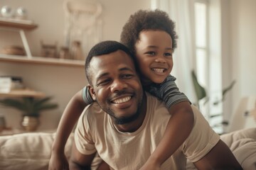 Obraz premium Nice young mixed-race dad and his gorgeous youngster cuddling on a sofa in their living room. Dad and son bonding and showing affection. Male child and single parent in the lounge