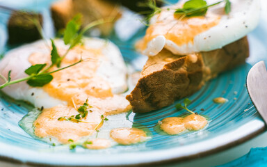Toast or slice of toasted bread with egg Benedict and hollandaise sauce on a turquoise plate. Beautiful presentation of the dish. Healthy and delicious breakfast. Selected focus.