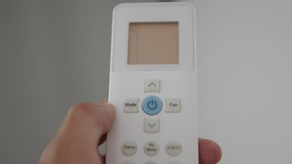 Close-up of remote control for controlling air conditioner. Unrecognizable man turns off climate control equipment remotely. Person turns on air conditioner at 21 degrees Celsius.