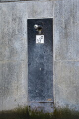 Small public faucet for drinking water on blue stone background wtih drinking water sign and green mossy growth on the ground and wall beneath