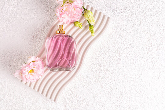 A chic bottle of women's perfume or cosmetic spray lies on a relief podium with austoma flowers. top view. A copy space. product presentation.