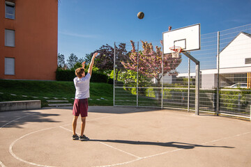 Young male basketball player playing basketball. Throwing the ball at playground. Precision shot